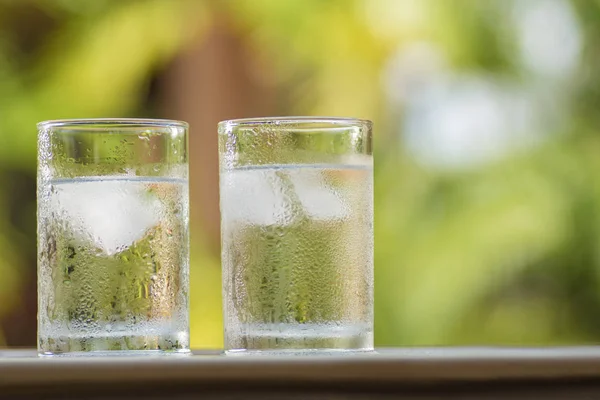 Transparent misted glasses with water and ice on table outdoors