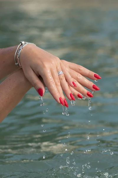 Female hands with white nail polish in the turquoise sea water on the background of the beach