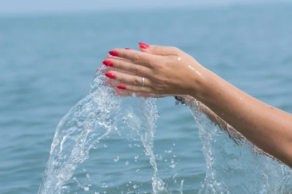 Female hands with white nail polish in the turquoise sea water on the background of the beach