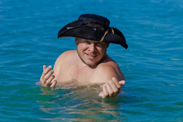 Emotional man in a black hat pirate posing in the surf in the water on the beach