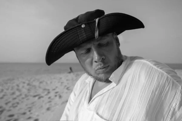 Emotional man in a black hat pirate posing  on the beach.
