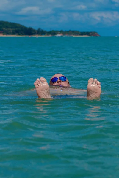 Tanned man with nude torso in sunglasses posing on the beach near the sea at sunset