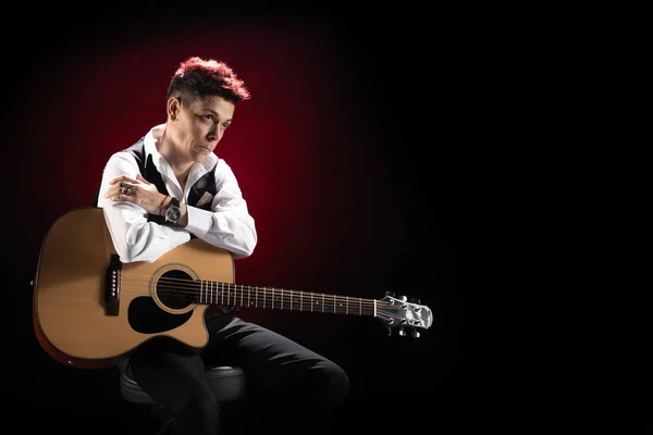 Woman musician with red hair in a black suit and white shirt posing with guitar on a black background