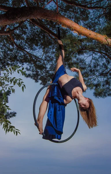 Girl performing acrobatic elements on the ring on the shore of the lake. Training aerial gymnastics