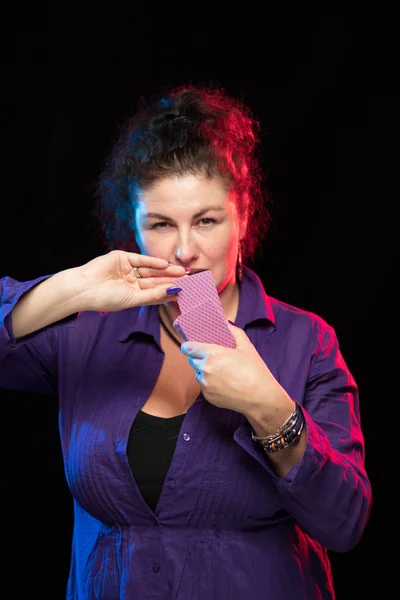 woman in purple clothes holds a deck of cards and shows tricks in a scenic light.