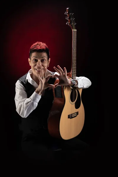 Woman musician with red hair in a black suit and white shirt posing with guitar on a black background
