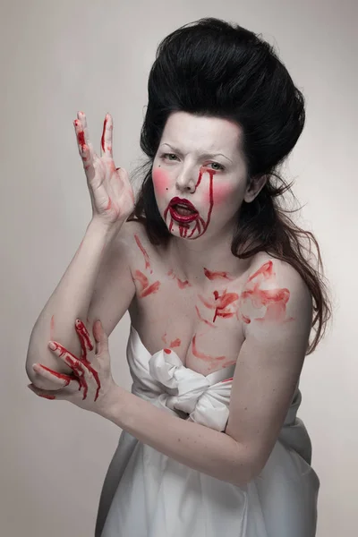 emotional actress brunette woman with pale skin in the role of vampire victims with blood on face on a white background in studio