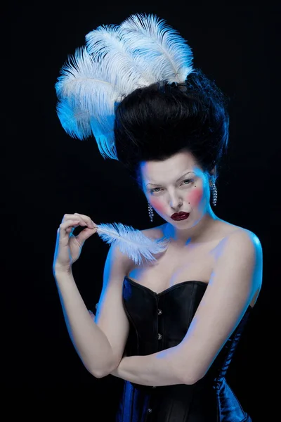 brunette woman with feathers in high hair and corset in old style on a black background