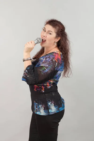 Emotional woman singer with microphone in hands singing and posing against light background