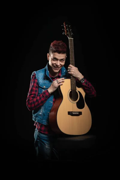 Woman musician with red hair in a denim suit with a guitar on a black background