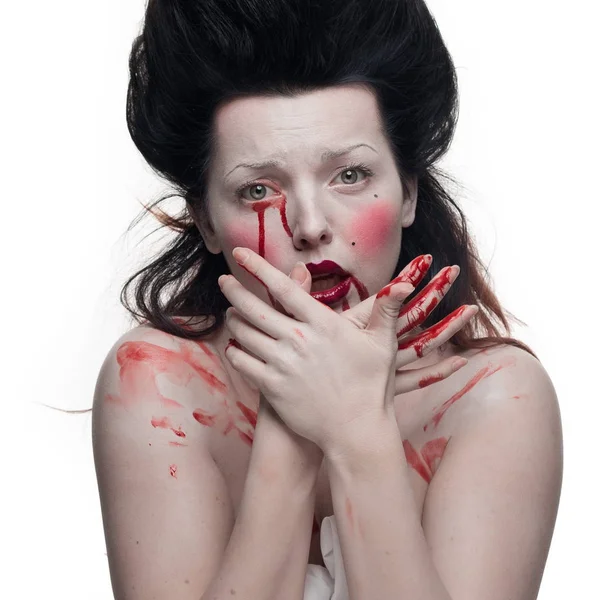 emotional actress brunette woman with pale skin as a vampire with blood on her face on a white background in studio