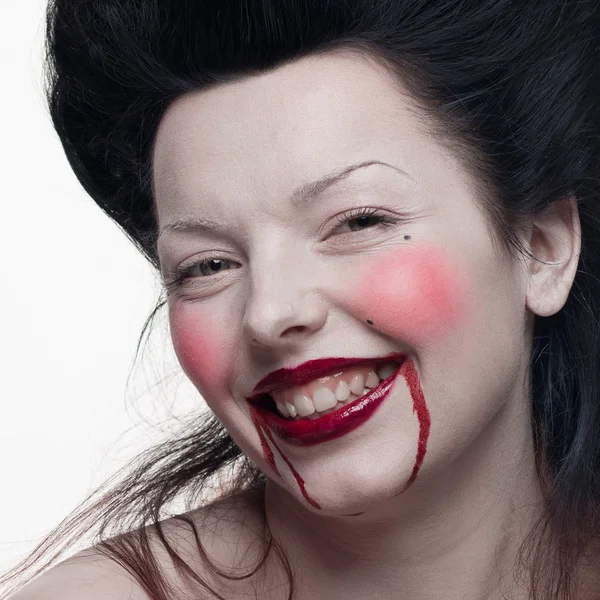 emotional actress brunette woman with pale skin as a vampire with blood on her face on a white background in studio