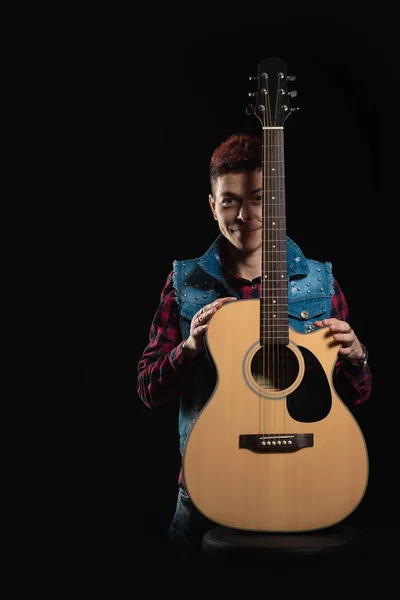 Woman musician with red hair in a denim suit with a guitar on a black background