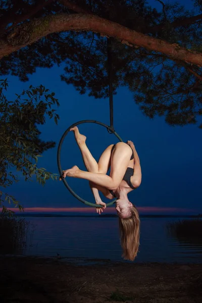 Girl performing acrobatic elements on the ring on the shore of the lake. Training aerial gymnastics