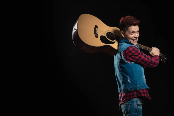 Woman musician with red hair in a denim suit with a guitar on a black background