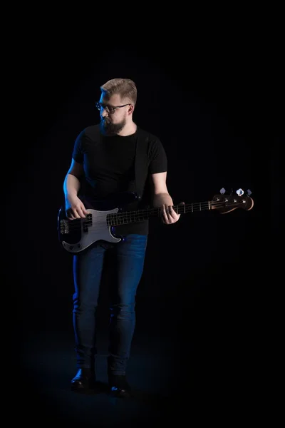 man in black clothes with guitar posing on black background