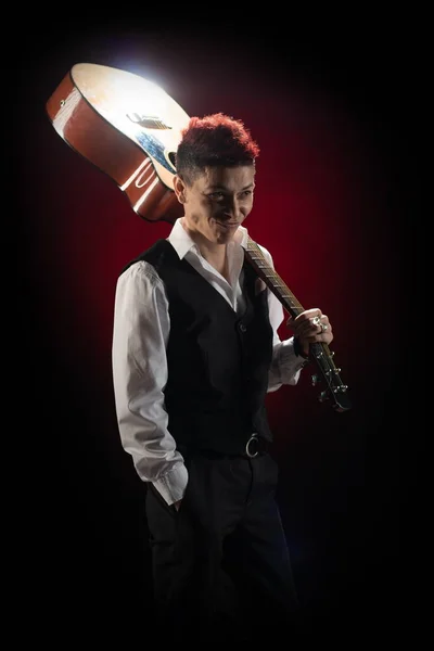 Woman musician with red hair in a black suit and white shirt posing with guitar on a black background