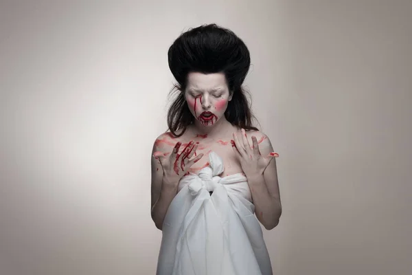 emotional actress brunette woman with pale skin in the role of vampire victims with blood on face on a white background in studio