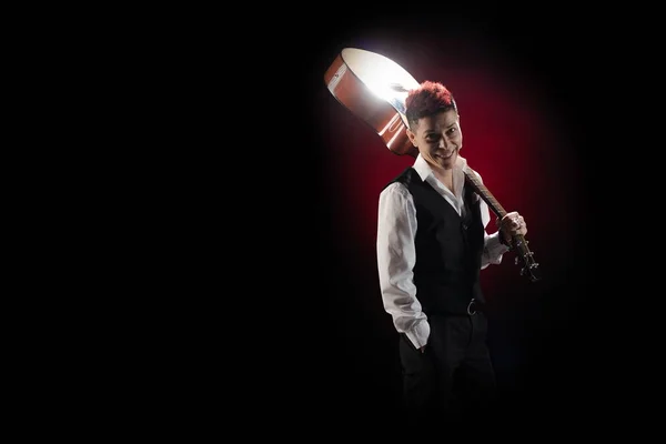 Woman musician with red hair in a black suit and white shirt posing with guitar on a black background