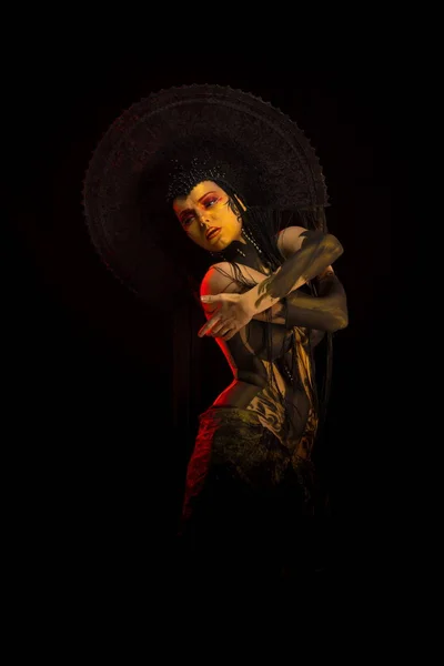 Actress woman in black headdress, body painting, golden figure on body and face, posing on black background