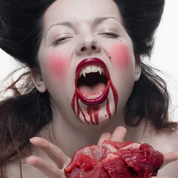 emotional actress brunette woman with pale skin as a vampire with blood on her face on a white background in studio