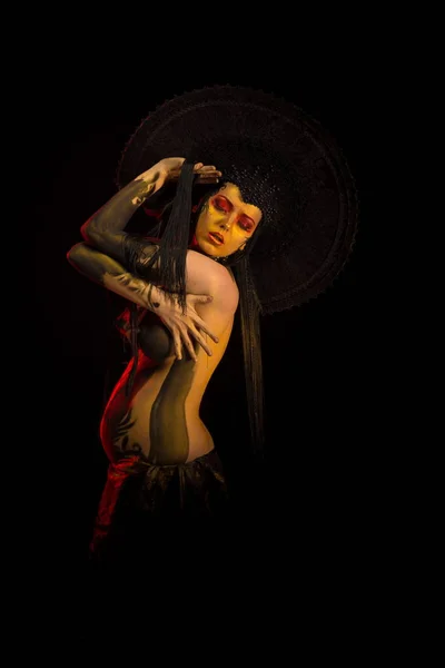 Actress woman in black headdress, body painting, golden figure on body and face, posing on black background