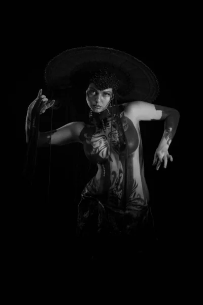 Actress woman in black headdress, body painting, golden figure on body and face, posing on black background