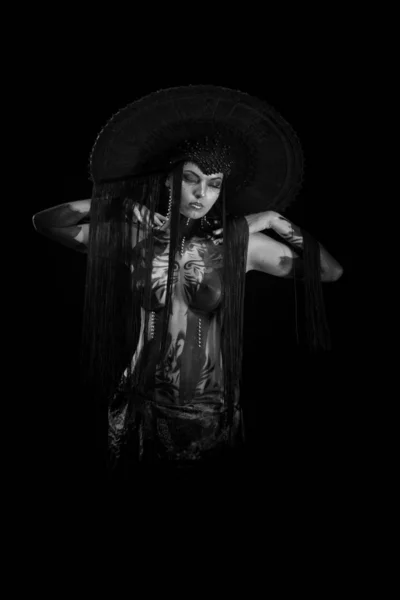 Actress woman in black headdress, body painting, golden figure on body and face, posing on black background