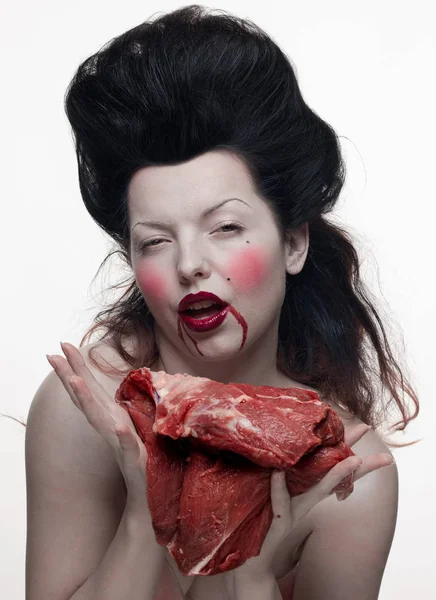 emotional brunette actress in the role of vampire with blood drops on face and a piece of bloody meat.