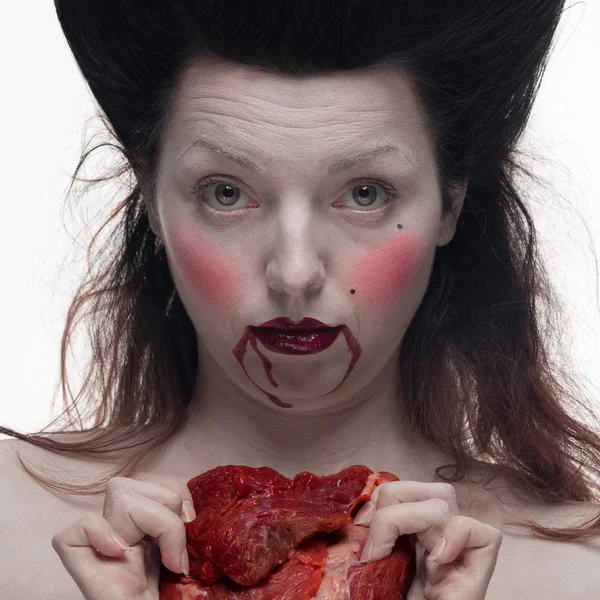 emotional actress brunette woman with pale skin as a vampire with blood on her face on a white background in studio