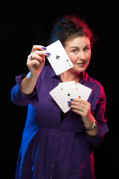 woman in purple clothes holds a deck of cards and shows tricks in a scenic light.