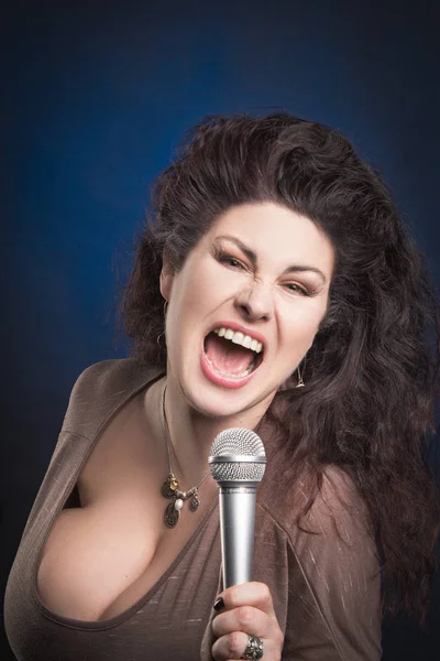 Emotional woman singer with microphone in hands singing and posing against blue background