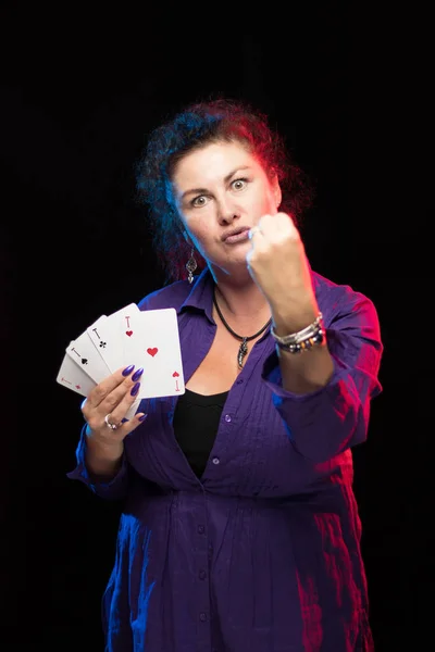 woman in purple clothes holds a deck of cards and shows tricks in a scenic light.