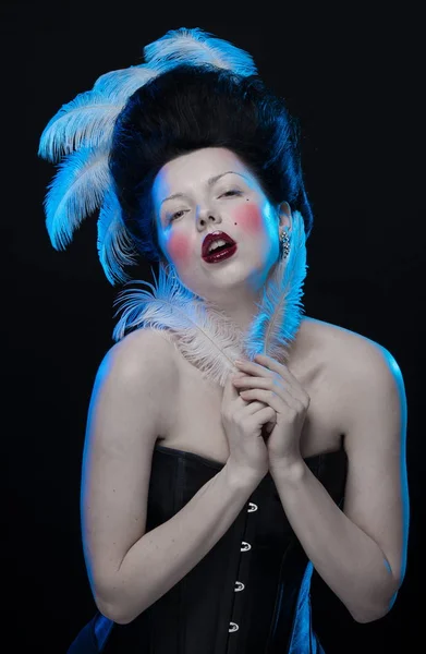 brunette woman with feathers in high hair and corset in old style on a black background