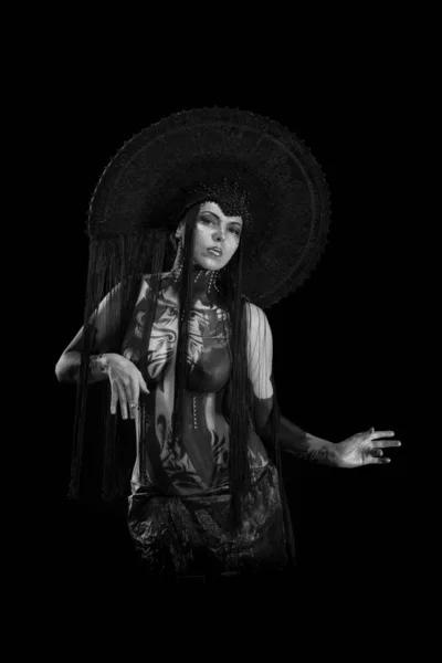 Actress woman in black headdress, body painting, golden figure on body and face, posing on black background