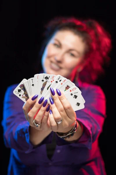 woman in purple clothes holds a deck of cards and shows tricks in a scenic light.