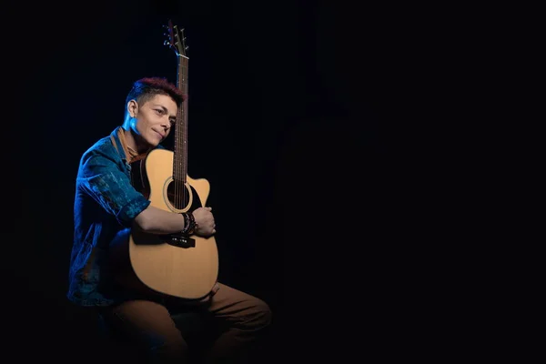 Woman musician with red hair in a denim suit with a guitar on a black background