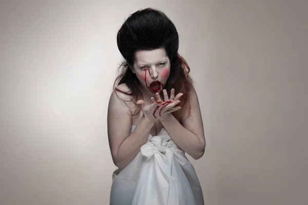 emotional actress brunette woman with pale skin in the role of vampire victims with blood on face on a white background in studio