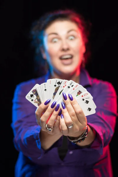 woman in purple clothes holds a deck of cards and shows tricks in a scenic light.