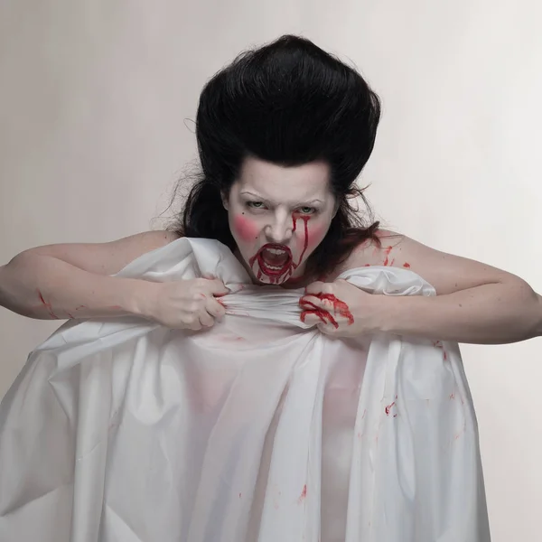 emotional actress brunette woman with pale skin in the role of vampire victims with blood on face on a white background in studio