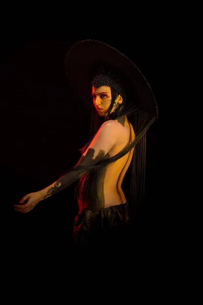 Actress woman in black headdress, body painting, golden figure on body and face, posing on black background