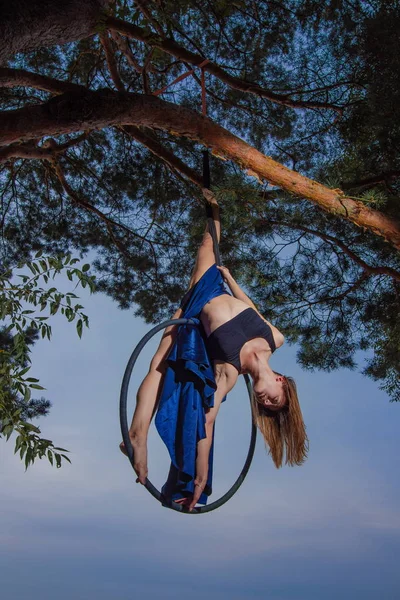 Girl performing acrobatic elements on the ring on the shore of the lake. Training aerial gymnastics