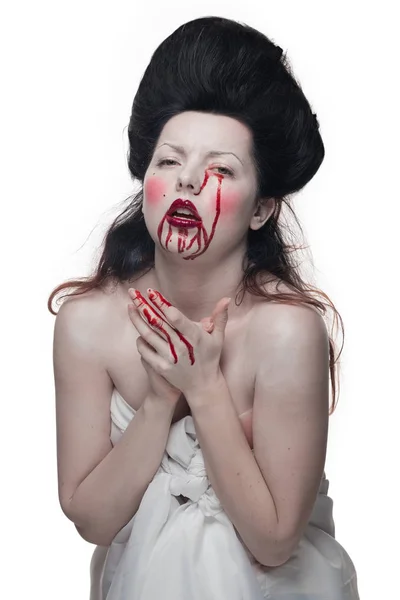 emotional actress brunette woman with pale skin in the role of vampire victims with blood on face on a white background in studio