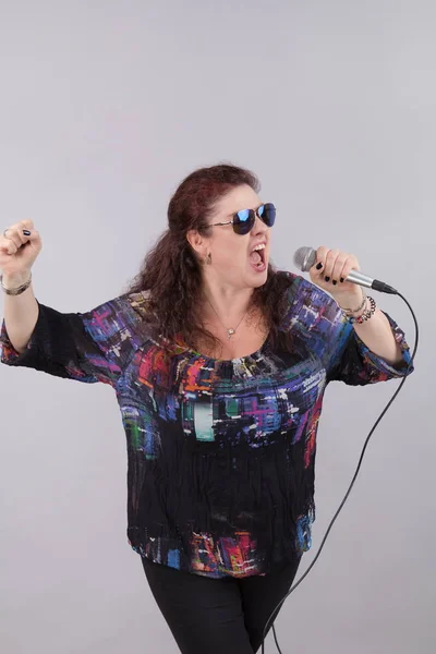 Emotional woman singer with microphone in hands singing and posing against light background