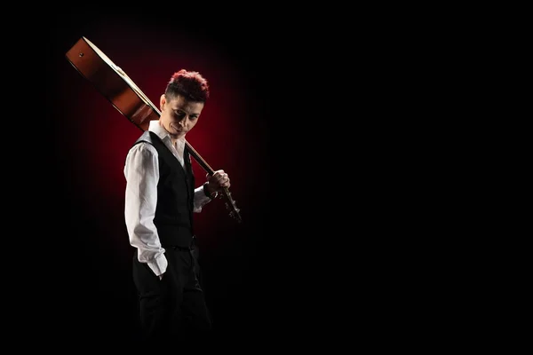 Woman musician with red hair in a black suit and white shirt posing with guitar on a black background