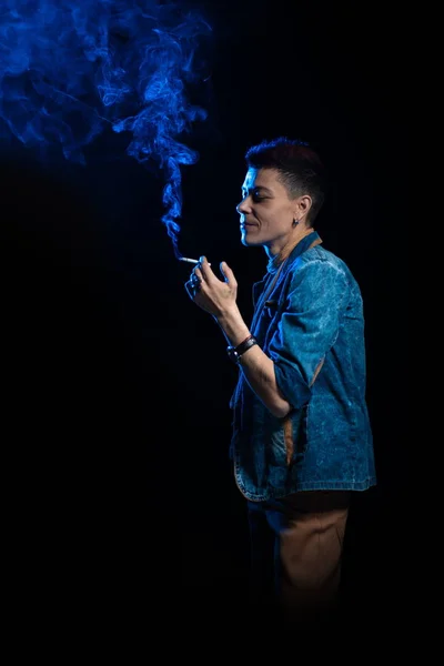 Woman with red hair in a denim suit smoking cigarette and posing on a black background