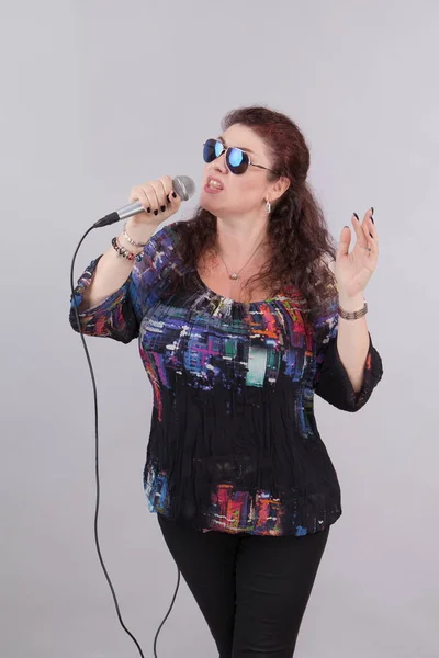 Emotional woman singer with microphone in hands singing and posing against light background