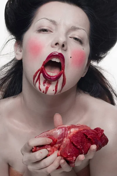 emotional brunette actress in the role of vampire with blood drops on face and a piece of bloody meat.