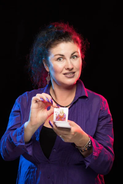 woman in purple clothes holds a deck of cards and shows tricks in a scenic light.