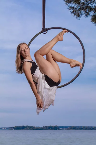 Girl performing acrobatic elements on the ring on the shore of the lake. Training aerial gymnastics